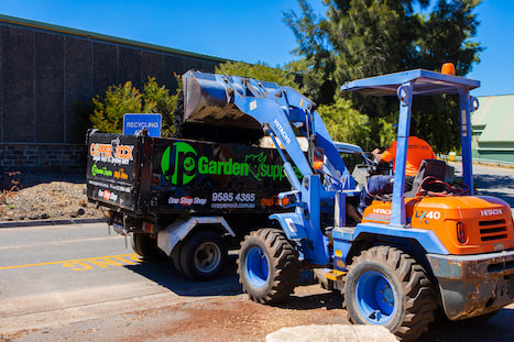 Backview of excavator unloading black garden supplies mulch into the back of a JP Garden supplies truck in Bayside
