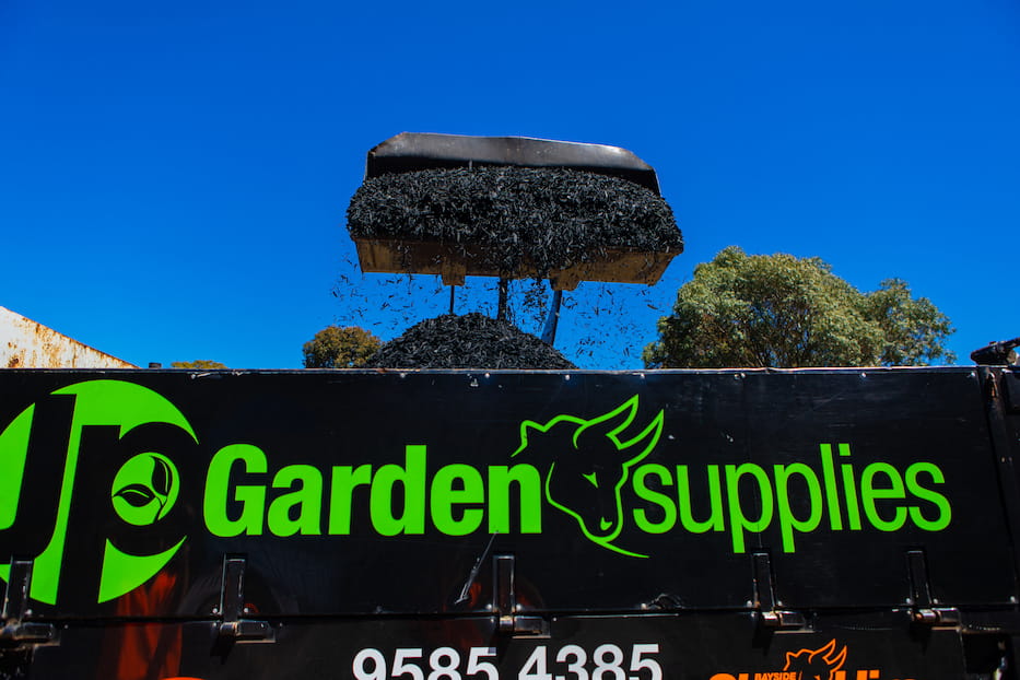 Excavator unloading black mulch garden supplies into black JP Garden supplies truck in Bayside